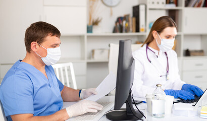 Obraz premium Doctors in protective medical masks enter patient data into the clinic computer network