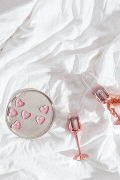 Pink colored shiny champagne glass in woman hand, burning candles as hearts on bed cloth. Minimal lifestyle aesthetic photo, Valentine's Day, romance relationship, love concept, romance evening