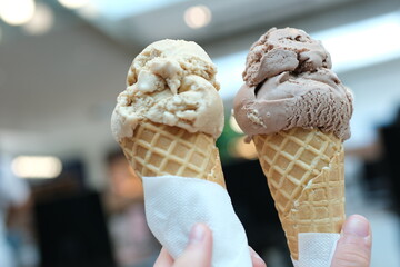 Two servings of ice cream cone on background of Mall, two girls clinking together with a brown, like glasses, game of communication, Friendship, eating delicious dessert. chocolate ice cream