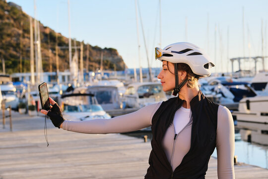 Beautiful fit woman cyclist taking a selfie with a mobile phone during training. Woman cyclist wearing cycling kit and white helmet riding a e-bike. Sports motivation image. Calp,Alicante,Spain.