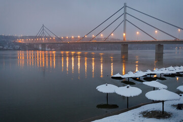 Flooded winter beach with umbrellas in water in night with suspension bridge