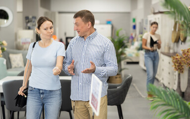 Obraz premium Interested man and woman strolling together through furniture showroom, curiously looking at various pieces for home and discussing choice