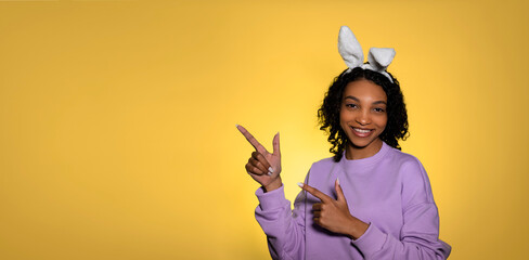 Easter studio shot with cute young woman in easter bunny ears pointing at empty space. Copy space...