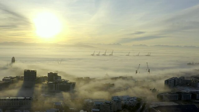 Drone, buildings and city in fog, ocean and sunrise in clouds with metro landscape, skyline and horizon. Environment, outdoor and urban expansion by sea, water and skyscraper in Cape Town with mist