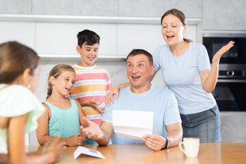Happy satisfied large family reading documents together while sitting at the table at home