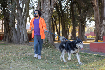 Young Mexican man with sunglasses, curly hair and beard, walking with his husky dog in the park