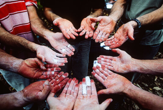 The chalk-covered and weathered hands of a group of rock climbers palm up and facing eachother in a circle