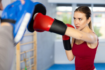 Fototapeta premium Adult man in punch mitts and young woman training boxing punches in studio