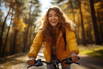 Young woman in yellow coat riding bicycle park. Active day.