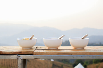 Fototapeta na wymiar Boiled rice with boiled egg, pork, coriander, and fried garlic in white bowl. Breakfast with beautiful natural landscape.