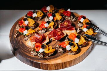 Gourmet Bruschetta with Prosciutto, Cheese, and Olives. Elegant bruschetta appetizers topped with prosciutto, melted cheese, roasted peppers, and black olives, presented on a round wooden platter.