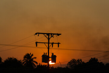 Silhouette of high voltage post with orange sky and cloud background and smoke