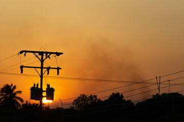 Silhouette of high voltage post with orange sky and cloud background and smoke
