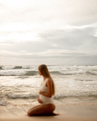 Fototapeta na wymiar Blurred image unfocused pregnant woman sit on the beach, focus at the ocean waves