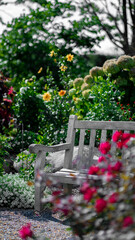 A white bench softly fades into a blurred background, allowing the vibrant green foliage and blossoming flowers to take center stage