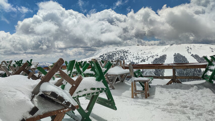 Stunning view of the mountain peak and ski slopes, white clouds and blue sky from the snow-covered closed ski coffee shop balcony.