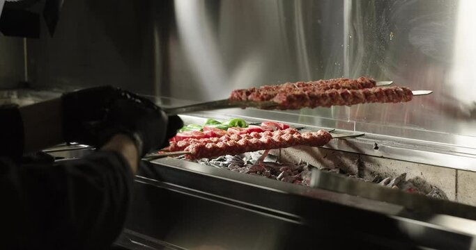 Chef puts raw kebabs on barbecue charcoal grill. Meat and vegetables on grill. Traditional Turkish kebab grilled on skewers