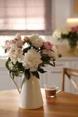 Beautiful peonies and cup of coffee on wooden table in kitchen
