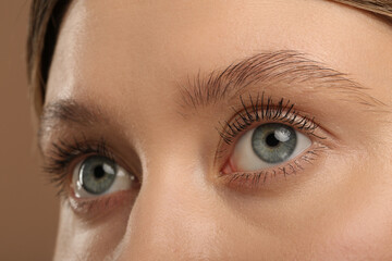 Naklejka premium Woman with long eyelashes after mascara applying against light brown background, closeup