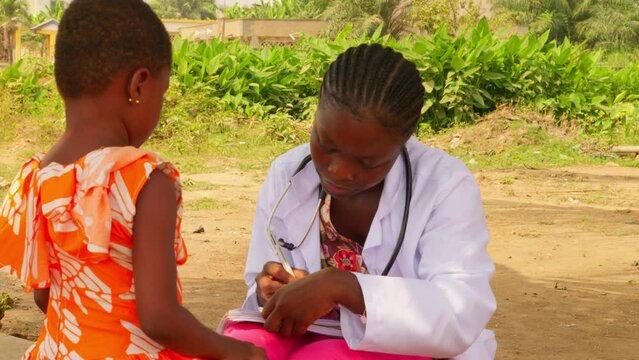 Close up of female black doctor measuring temperature making diagnosis to a young girl child in remote clinic in Africa, close up of doc in white lab slow motion