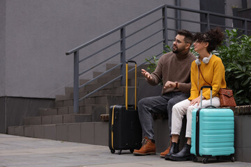 Being late. Worried couple with suitcases sitting on bench outdoors, space for text