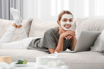 Young woman with face mask using laptop on sofa at home. Spa treatments