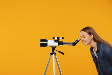 Young astronomer looking at stars through telescope on orange background, space for text