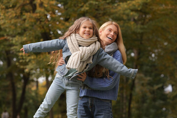 Happy mother playing with her daughter in autumn park