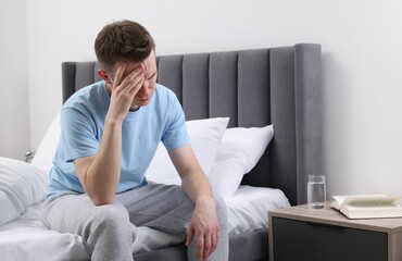 Sad man suffering from headache on bed indoors, space for text