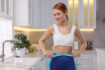 Slim woman measuring waist with tape in kitchen. Weight loss
