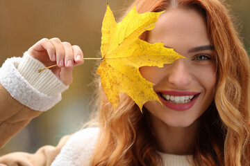Portrait of smiling woman covering eye with autumn leaf outdoors, closeup