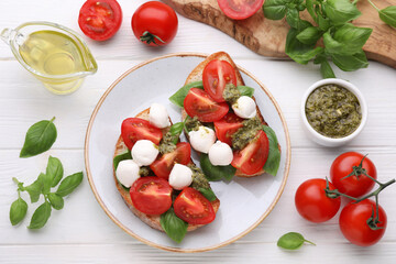 Delicious Caprese sandwiches with mozzarella, tomatoes, basil and pesto sauce on white wooden table, flat lay