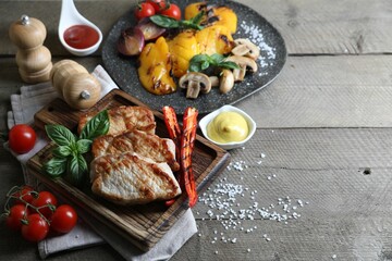 Delicious grilled meat and vegetables served on wooden table. Space for text
