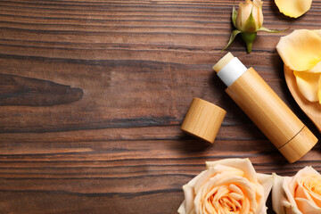 Fototapeta na wymiar Lip balm and roses on wooden background, flat lay. Space for text