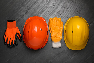 Hard hats and gloves on black table, flat lay. Safety equipment