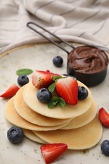 Delicious pancakes with berries and chocolate spread on plate, closeup