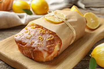 Wrapped tasty lemon cake with glaze on wooden board, closeup