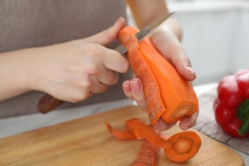 Woman peeling fresh carrot with knife at white table, closeup