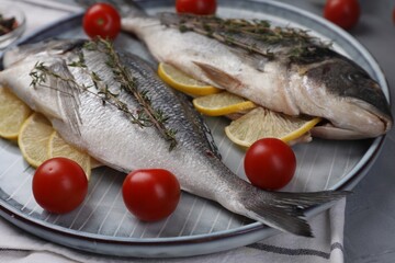Raw dorado fish with thyme, lemon slices and tomatoes on table, closeup