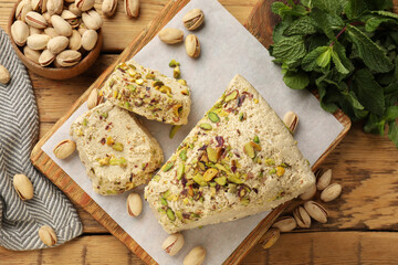 Tasty halva with pistachios and mint on wooden table, flat lay