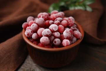 Frozen red cranberries in bowl on wooden table, closeup