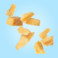Tasty parmesan cheese falling on light blue background
