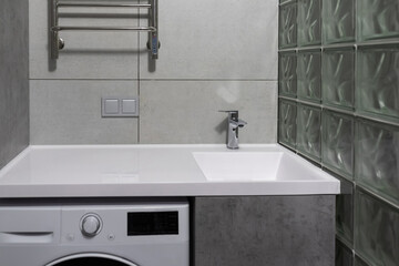 Modern bathroom interior with minimalist lighting. Close-up Washing machine, sink with cabinet and towel dryer
