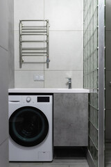 Modern bathroom interior with minimalist lighting. Washing machine, sink with cabinet and towel dryer