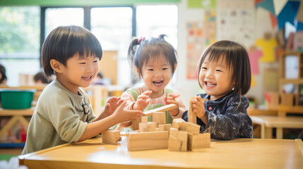 日本の幼稚園児3人が私服で木の積み木を使って笑顔で遊んでいる写真、背景保育ルーム、木育/幼児教育 - obrazy, fototapety, plakaty