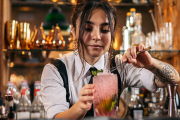 Female bartender pouring a cocktail and decorating it with garnish