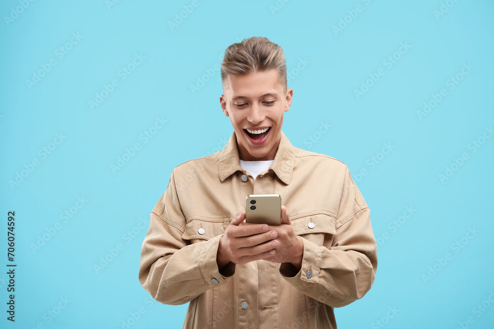 Poster Emotional young man sending message via smartphone on light blue background