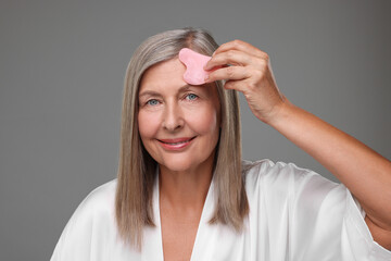 Woman massaging her face with rose quartz gua sha tool on grey background