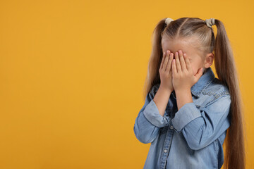 Resentful girl covering her face with hands on orange background. Space for text