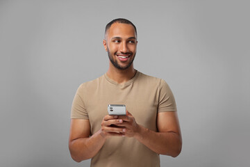 Happy man sending message via smartphone on grey background